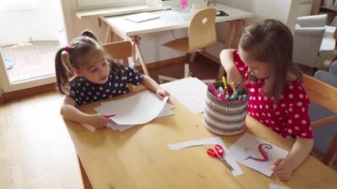 Küçük kızlar salgın sırasında evlerinde kağıda resim çizerler.