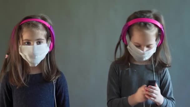 Two adorable girls in a mask with headphones listen to music — Stock Video