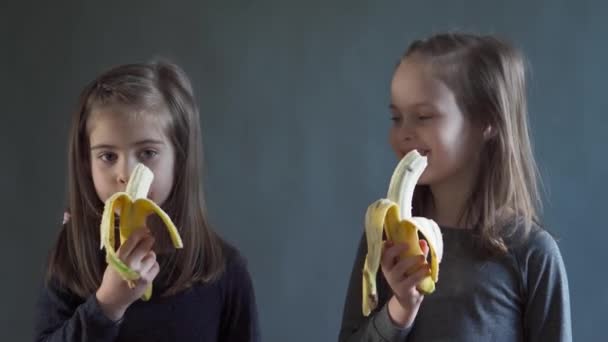 Duas meninas adoráveis estão comendo uma deliciosa banana — Vídeo de Stock