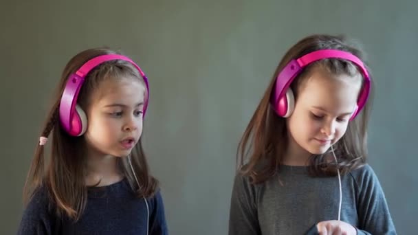 Dua gadis menggemaskan dengan headphone mendengarkan musik dan menari — Stok Video