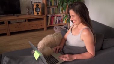 Kadın evde çalışıyor ve salgın sırasında köpekle yavaş çekimde oynuyor.