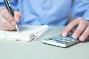 Hesap makinesi kullanma ve bir not defteri yazma adam.