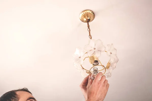 Electrician man changing light bulbs in chandelier.