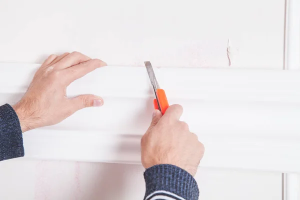 Man with knife cutting ceiling skirting. — Stock Photo, Image