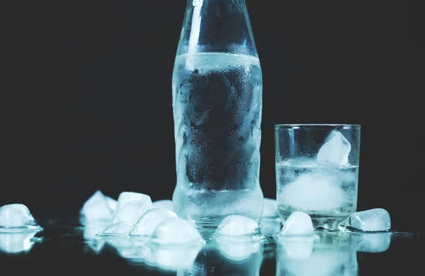 Flaska vodka med ett glas och ices på svart bakgrund. — Stockfoto
