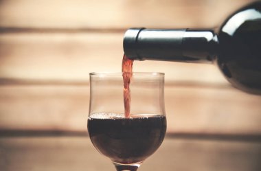 Ahşap arka plan üzerinde bir bardak içine kırmızı şarap dökme.