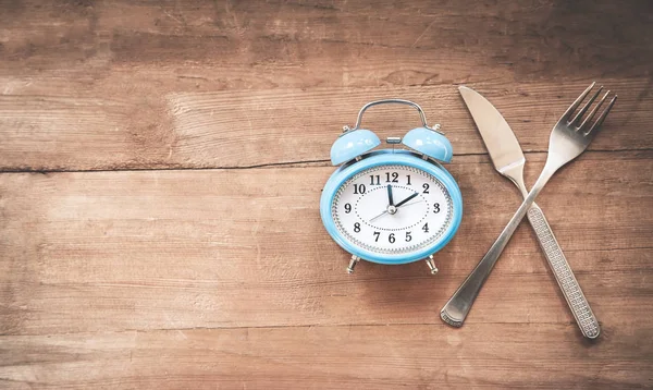 Ceas deşteptător cu furculiţă şi cuţit pe masă. E timpul să mănânci . — Fotografie, imagine de stoc