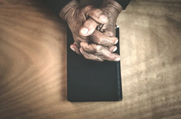 Old hands on the bible on a wood background. — Stock Photo, Image