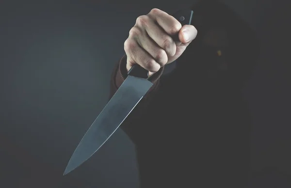Crimen encapuchado mostrando cuchillo en habitación oscura . — Foto de Stock