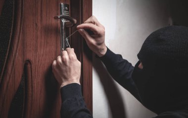 Siyah maskeli bir soyguncu kapıyı açmaya çalışıyor..