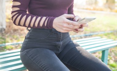 Park yerinde oturan ve telefon kullanan bir kadın..