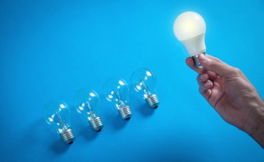 Mavi arka planda ampulü tutan erkek el..