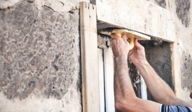 Pencerenin yanındaki duvarı sıvamak için mala kullanan sıva ustası.