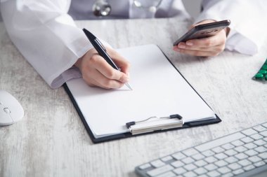 Doktor, klinikteki bir panoya yazı yazıp akıllı telefon kullanıyor.. 