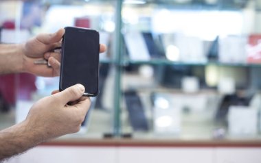 Elektronik mağazasında akıllı telefon gösteren erkek eller.