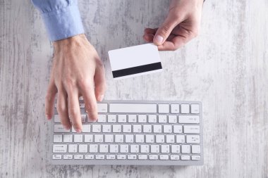 Kredi kartı tutan ve klavyeyle yazan bir adam. Çevrim içi ödeme ve alışveriş