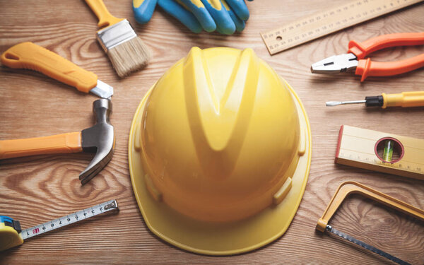 Рабочие инструменты со шлемом и перчатками на деревянном фоне
.