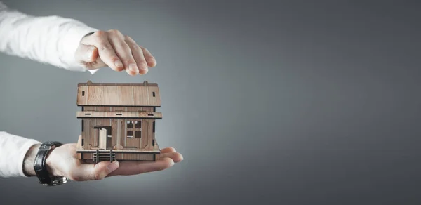 Male hands protect wooden house model.