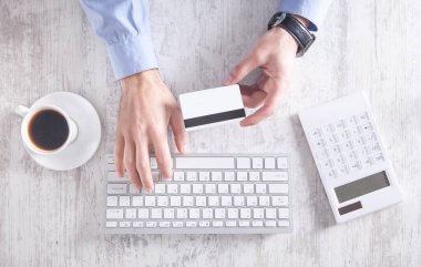 Kredi kartı tutan ve klavyeyle yazan adam..