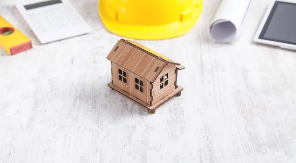 Wooden house model with a helmet, tablet, calculator, level, and document.