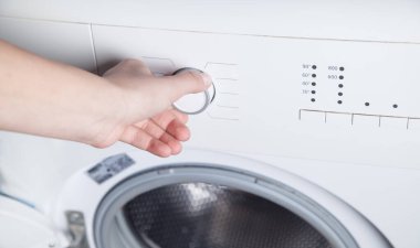 Kız eli çamaşır makinesinin düğmesini çeviriyor..