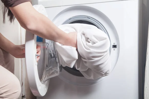 Çamaşır makinesine çarşaf koyan kız.