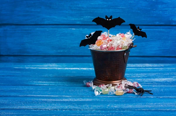 Cubo de dulces de Halloween, murciélagos de papel y araña de goma en woo azul — Foto de Stock