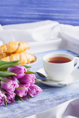 Kruvasan çay mor laleler mavi ahşap tepsi ile Kahvaltı.