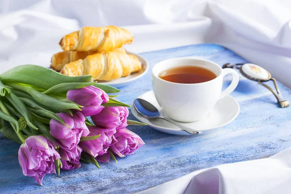 Ontbijt met croissants thee paarse tulpen op blauwe houten dienblad. Rechtenvrije Stockafbeeldingen