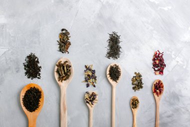 Tahta kaşık ile farklı çay yaprakları üzerinde gri beton backgro