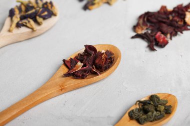 Tahta kaşık ile farklı çay yaprakları üzerinde gri beton backgro