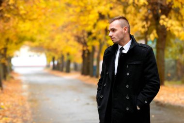 Sonbahar yağmur ormanı içinde siyah montlu çekici adam. 