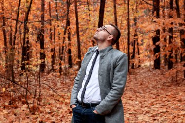 Sonbahar ormandaki gri paltolu modern yakışıklı çekici insan. Moda ve giyim kavramı. Metin için özgür yer.