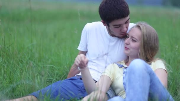 Pareja joven enamorada acostada en el césped en el campo, abrazándose y hablando . — Vídeos de Stock