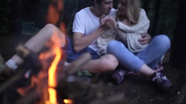 Νεαρό ζευγάρι κάθεται σε μια πυρκαγιά στο δάσος. Ο τύπος φιλιά το κορίτσι. — Αρχείο Βίντεο