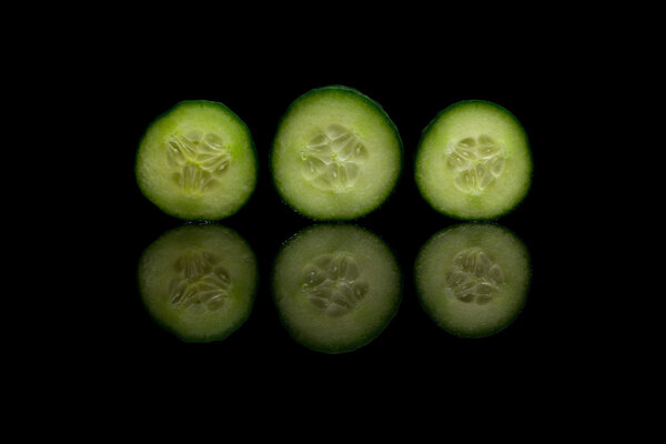 Three cucumbers on black reflective background