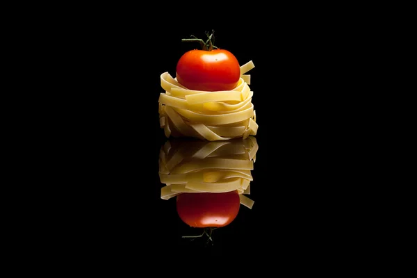 Nest pasta with red tomato black reflective background — Stock Photo, Image