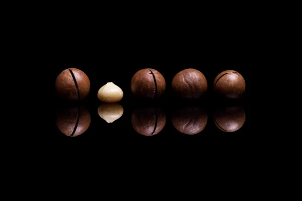 反射する黒い背景に分離された 5 つのマカダミア ナッツ ロイヤリティフリーのストック画像