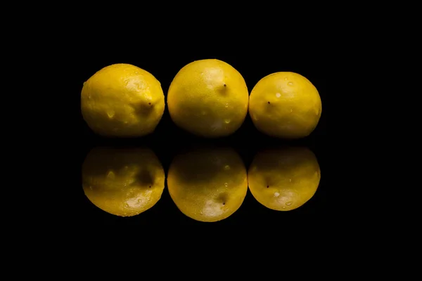 Три полностью изолированных желтых лимона на черном фоне — стоковое фото