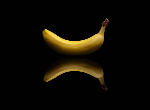 Singola banana gialla su sfondo nero riflettente — Foto Stock