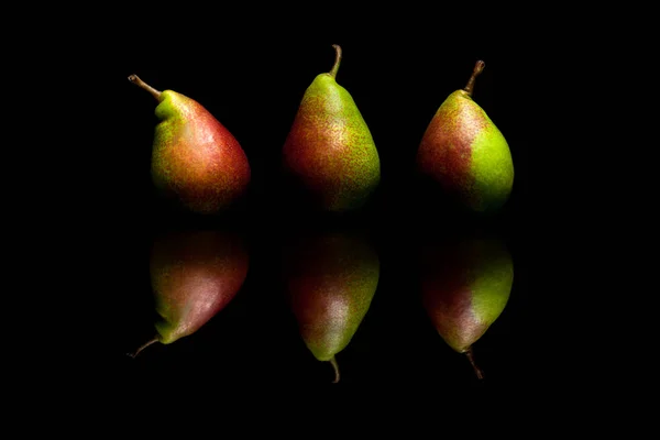 Τρία ολόκληρα κόκκινα και πράσινα αχλάδια απομονώνονται σε μαύρο φόντο — Φωτογραφία Αρχείου