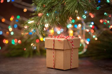 Noel ağacı ve ışıklarının arka planında bir hediye olan Kraft kutusu.