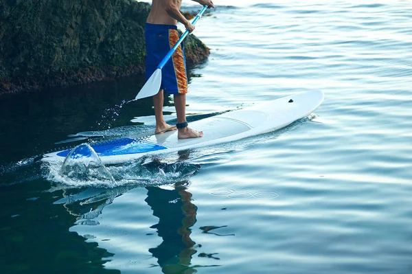 海の中でパドリングを楽しんでいる若い男 Sup 石の近くのパドルボードで朝の男の訓練 — ストック写真