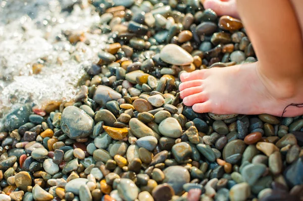 Child\'s feet on a beach in small color pebble in a summer sunny day. Holiday on a seashore. Vacation.