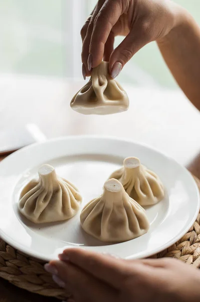 Georgische traditionelle Khinkali auf weißem Teller. Ein Chinkali in Frauenhand. — Stockfoto