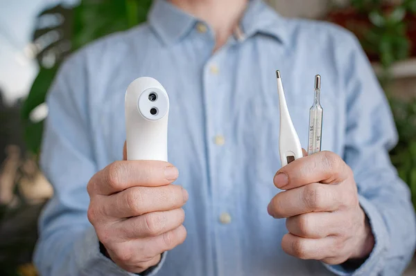 Çeşitli termometreler tutun. Merkür, dijital ve temassız termometreler. İnsanlar ve sağlık hizmetleri konsepti. Coronavirus. Arkaplanda yeşil yapraklar