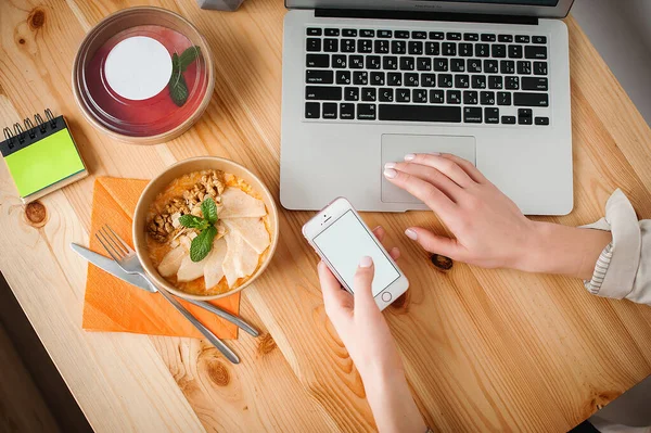 Bir kadın yemek yer ve evde çalışır. Yakın plan. Üst Manzara. Akıllı telefonda metin için boşluk
