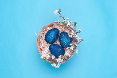 Mor arka planda çiçekler olan sepetteki gök mavisi paskalya yumurtaları. Yatay fotoğraf. Üst Manzara Flatley. Üst Manzara. Fotoğrafın ortasındaki nesne..