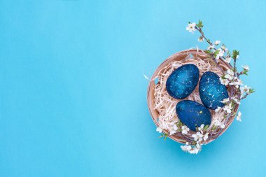 Mor arka planda çiçekler olan sepetteki gök mavisi paskalya yumurtaları. Yatay fotoğraf. Üst Manzara Flatley. Üst Manzara. Fotoğrafın sağ tarafında nesne var.