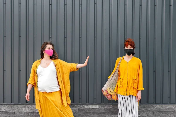Uzakta koruyucu maskeli ve sarı elbiseli iki kadın duruyor. Sosyal uzaklık kavramı. Siyah arkaplan